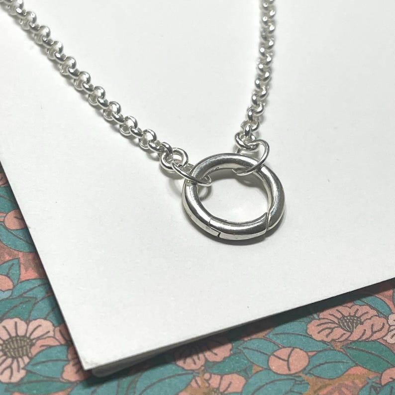 Op de afbeelding: Een zilveren ketting met een zilveren ringgesp. De ketting is een delicate, fijne ketting.