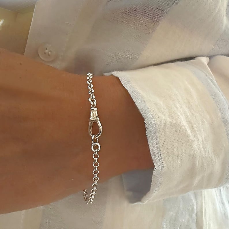May include: A silver chain bracelet featuring a polished finish and a central lobster claw clasp. The bracelet is constructed from small, uniform circular links that connect to a larger, secure lobster clasp mechanism, creating a continuous loop.
