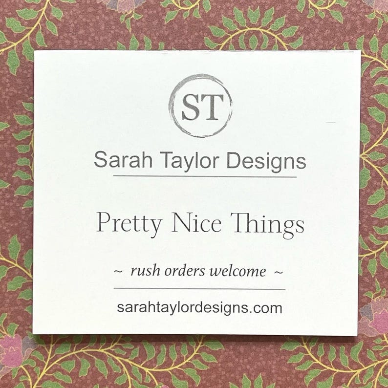 May include: A white business card with the text "Sarah Taylor Designs" and "Pretty Nice Things" in a serif font. The card also includes the text "~ rush orders welcome ~" and the website address sarataylordesigns.com.