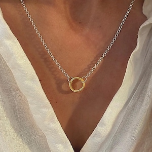 May include: A silver chain necklace featuring a single, small, polished gold-tone circular pendant at the centre. The necklace is composed of delicate, interconnected silver links that form a simple, continuous loop around the neck area.