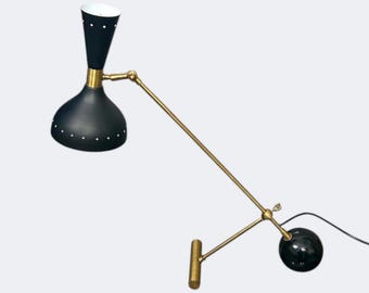 May include: A black and gold mid-century modern wall lamp. The lamp features a black shade with white dot accents, a gold-colored arm, and a black sphere base. The lamp is designed to be mounted on a wall.