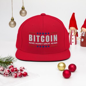 May include: Red and white baseball cap with the text "Bitcoin Make Money Great Again" embroidered on the front. The text is in white with blue stars.