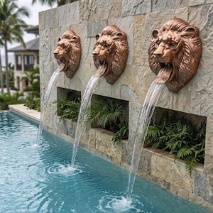 May include: Three copper-colored lion head wall fountains mounted on a rectangular stone wall. Each lion head features an open mouth with a continuous stream of water flowing into a swimming pool below. Green ferns are planted in recessed niches.