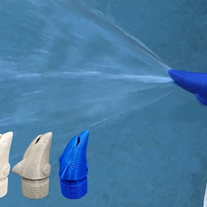 May include: A blue shark-shaped pool fountain nozzle attached to a pool wall, spraying a stream of water. Three additional shark-shaped nozzles are shown separately in white, light tan, and blue, each featuring a threaded base for installation.