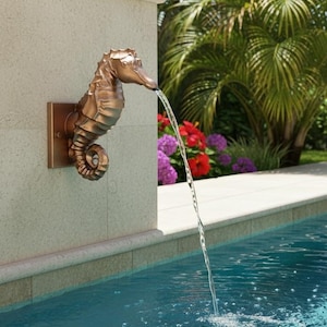 May include: A bronze-colored seahorse wall fountain mounted on a light-colored stone pillar. The seahorse is positioned horizontally with its snout pointing downward, emitting a steady stream of water into a swimming pool below.