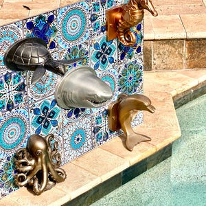 May include: A collection of five wall-mounted marine animal sculptures including a dark gray sea turtle, a silver shark head, a bronze seahorse, a bronze dolphin, and a bronze octopus, all displayed on a wall of blue and white patterned tiles.