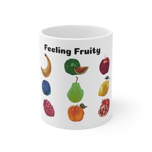 May include: White ceramic mug with the text "Feeling Fruity" printed in black. The mug features a colourful illustration of various fruits, including a banana, watermelon, apple, plum, pear, lemon, raspberry, peach, and pomegranate.