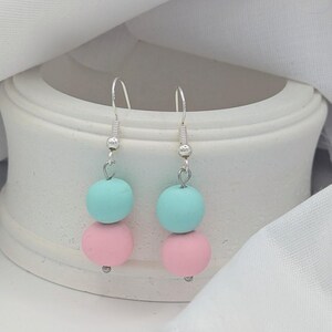 May include: A pair of pastel-coloured earrings. Each earring features a light blue sphere stacked on top of a pink sphere. The earrings hang from silver-coloured fish hook ear wires.