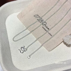 Puede incluir: Un collar de cadena en tono plateado con un dise&ntilde;o de eslabones delicados y un cierre de mosquet&oacute;n seguro. El collar se muestra sobre una bolsa de tela beige claro con el texto 07&Rice kindness for wellness y el c&oacute;digo XBU013Y-22.