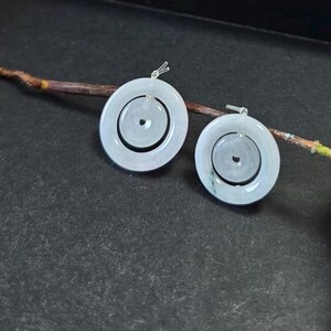 May include: A pair of circular earrings featuring a pale, translucent white stone with a smooth, polished finish. Each earring consists of a larger outer ring and a smaller inner ring connected by a silver-toned metal post and bail mechanism.