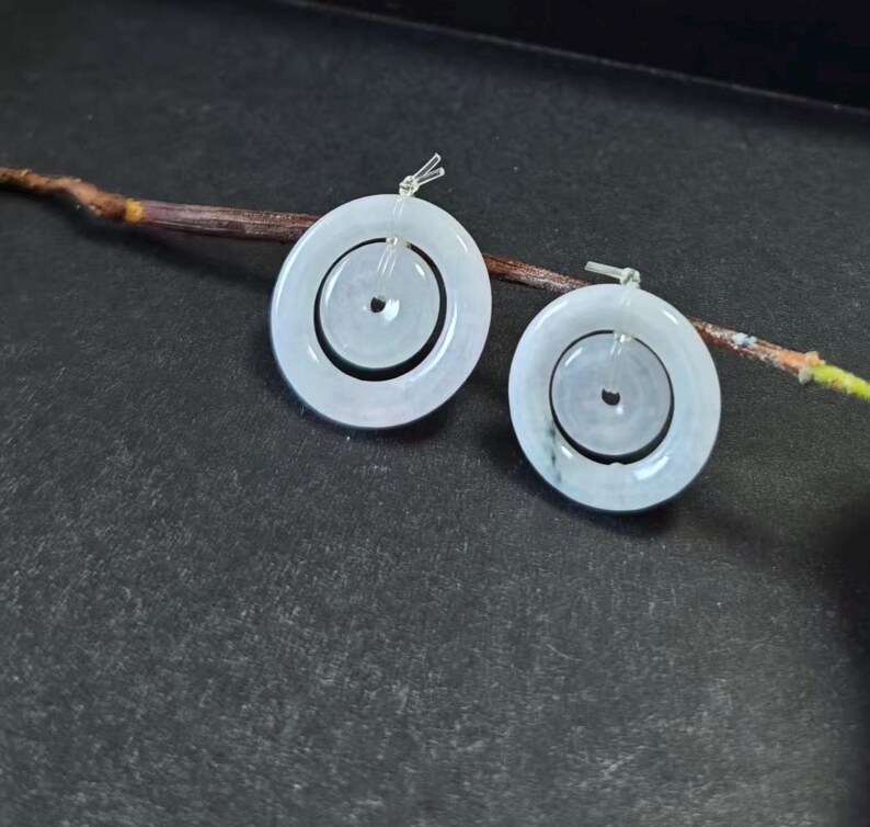 May include: A pair of circular earrings featuring a pale, translucent white stone with a smooth, polished finish. Each earring consists of a larger outer ring and a smaller inner ring connected by a silver-toned metal post and bail mechanism.