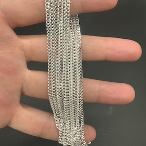 Puede incluir: Un collar de cadena de color plateado que presenta una serie de eslabones planos e interconectados que crean una textura met&aacute;lica continua y reflectante. La cadena est&aacute; compuesta por m&uacute;ltiples hilos con el mismo dise&ntilde;o de eslabones.