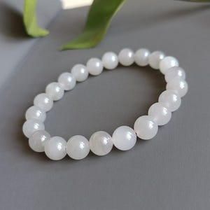 May include: A white gemstone bracelet with round beads. The bracelet is made of white moonstone beads.