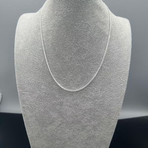 Puede incluir: Un collar de cadena de metal de color plateado con un dise&ntilde;o delicado de eslabones tipo barbada. El collar se muestra en una ca&iacute;da circular simple, exhibiendo los eslabones uniformes y reflectantes que forman un bucle met&aacute;lico continuo y pulido.