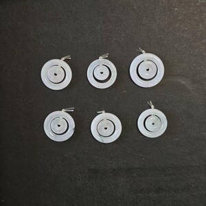 May include: Six circular pendants featuring a double-ring design. Each pendant consists of a larger outer ring and a smaller inner ring, both crafted from a pale, translucent white material. Each piece includes a small silver-toned metal bail.