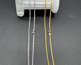 Puede incluir: Dos collares, uno plateado y otro dorado, cuelgan de una columna decorativa blanca. El collar plateado está a la izquierda y el collar dorado a la derecha. Ambos collares tienen un diseño de cadena delicado y se muestran sobre un fondo oscuro.