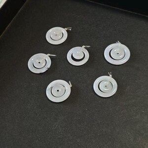 May include: Six circular white jade pendants, each featuring a smaller concentric ring suspended within a larger outer ring. These smooth, polished stone charms have a translucent appearance and include a small silver-toned metal bail at the top.