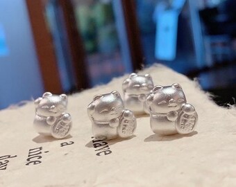 Puede incluir: Cuatro pequeños dijes plateados con forma de oso están dispuestos sobre una superficie clara. Cada dije está esculpido en posición sentada, sosteniendo una moneda. Los dijes tienen un acabado liso y reflectante. Las palabras "a nice day" son parcialmente visibles.