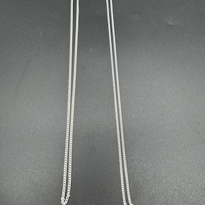 Puede incluir: Dos cadenas de metal de color plateado id&eacute;nticas, cada una con un dise&ntilde;o de eslabones finos tipo barbada. Ambas cadenas son largas y delgadas, est&aacute;n suspendidas verticalmente y terminan con un peque&ntilde;o mecanismo de cierre seguro en la parte superior.