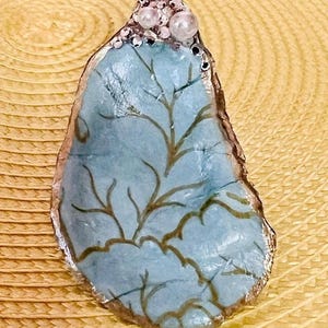 May include: A blue and gold oyster shell with a decorative design and a cluster of white and clear rhinestones on top.