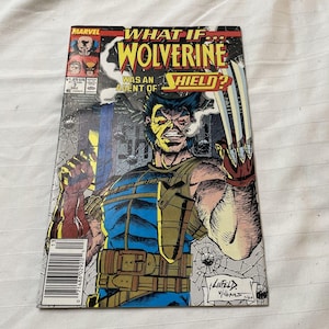 Puede incluir: Portada de cómic con Wolverine como agente de S.H.I.E.L.D. La ilustración muestra a Wolverine con sus garras extendidas, vistiendo un uniforme azul y marrón. El título dice "What If... Wolverine Was an Agent of S.H.I.E.L.D?" con el logo de Marvel arriba.