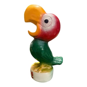 May include: A colorful parrot statue with a yellow beak, red head, and green body. The parrot is perched on a white base with the word "Cafe" in red. The statue is a decorative item.