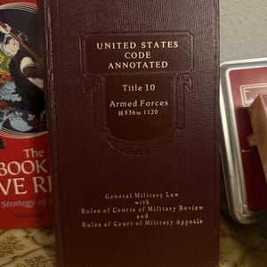 May include: A maroon hardcover book titled "UNITED STATES CODE ANNOTATED" with "Title 10 Armed Forces" visible. The book also includes text about military law and court rules.