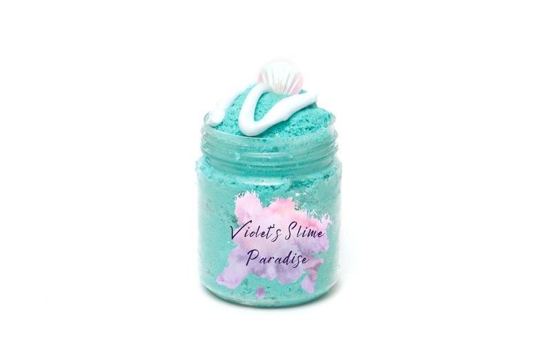 May include: A teal blue slime in a clear glass jar with a white swirl on top and a white seashell. The jar has a label that says "Violet's Slime Paradise".