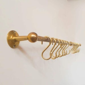 May include: A brass-colored kitchen rail with a series of S-shaped hooks. The rail is mounted on a wall and features a round ball at the center. The hooks are evenly spaced along the rail, providing a stylish storage solution.
