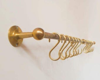 May include: A brass-colored kitchen rail with a series of S-shaped hooks. The rail is mounted on a wall and features a round ball at the center. The hooks are evenly spaced along the rail, providing a stylish storage solution.