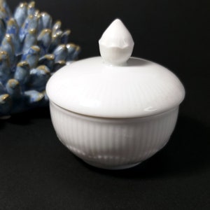 May include: White ceramic sugar bowl with a lid. The lid has a small knob on top. The bowl has a ribbed design.