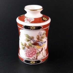 Könnte beinhalten: Eine kleine, weiße Porzellanvase mit einem roten und schwarzen geometrischen Muster und einem floralen Muster mit einem Vogel. Die Vase hat einen goldenen Rand.