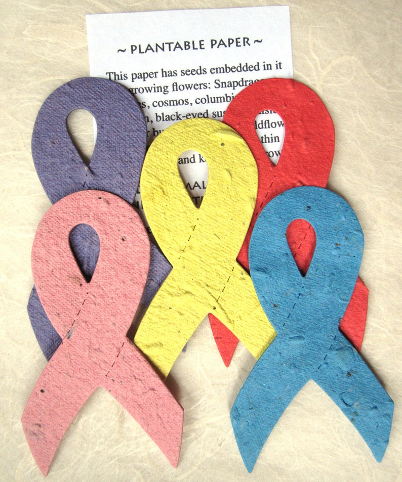 K&ouml;nnte beinhalten: Vier pflanzbare Papierbandformen in verschiedenen Farben: Lila, Rosa, Gelb und Blau. Das Papier enth&auml;lt eingebettete Samen und kann gepflanzt werden, um Blumen wachsen zu lassen. Der Text auf dem Papier lautet "Pflanzbares Papier" und listet die Arten von Blumen auf, die wachsen k&ouml;nnen.