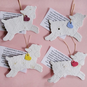 Peut inclure: Quatre ornements en papier blanc en forme d'agneau avec une &eacute;tiquette en forme de c&oelig;ur attach&eacute;e &agrave; chacun. Les &eacute;tiquettes sont de couleurs diff&eacute;rentes&nbsp;: rose, bleu, jaune et rouge. Le papier est plantable et contient des graines pour faire pousser des fleurs. Le texte sur les &eacute;tiquettes indique "Plantable Paper" et comprend des instructions pour planter le papier.