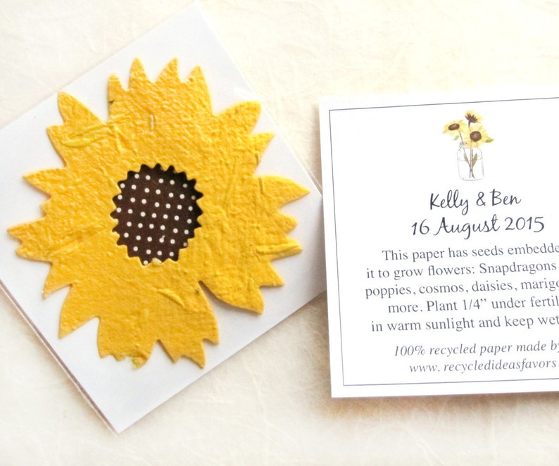 May include: A yellow paper sunflower with a brown and white polka dot center. The paper has embedded seeds to grow flowers like snapdragons, poppies, cosmos, daisies, and marigolds. The paper is 100% recycled and made by Recycledideasfavors.com. The text on the paper reads "Kelly & Ben 16 August 2015".
