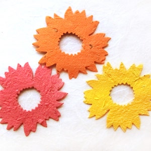 May include: Three paper flower embellishments in orange, pink, and yellow. Each flower has a circular center and a ring of petals.