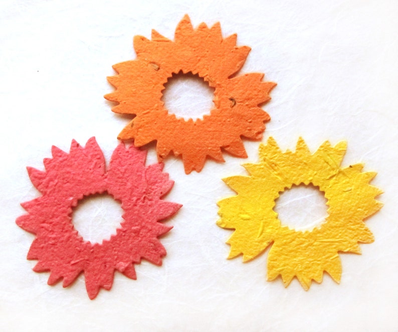 May include: Three paper flower embellishments in orange, pink, and yellow. Each flower has a circular center and a ring of petals.