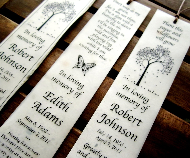 May include: Three white bookmark designs with black ink. Each bookmark features a tree with leaves and a butterfly. The text on the bookmarks reads "In loving memory of" followed by a name and dates. The text on the bottom bookmark reads "Plant this paper and wildflowers will grow".