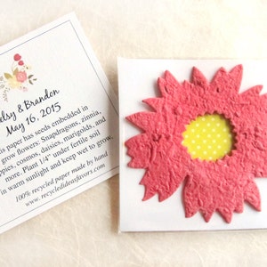 May include: A pink paper flower with a yellow center and white polka dots. The flower is packaged in a clear plastic bag with a white card that reads "Kelsy & Brandon May 16, 2015" and includes information about the flower seeds embedded in the paper.