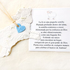 Peut inclure: Un agneau en papier blanc avec un c&oelig;ur bleu attach&eacute;. L'agneau est suspendu &agrave; une ficelle. Le texte sur la carte dit : "La fe es una peque&ntilde;a semilla Plantada profundo dentro del alma, la semilla comienza a crecer. Alimentada por la confianza en Dios se abre silenciosamente, como una fragante flor. Extiende sus ra&iacute;ces para encontrar un hogar, enriquecido por el gran poder de Dios. Planta estas semillas de cualquier manera para celebrar el bautizo de Andreas!"