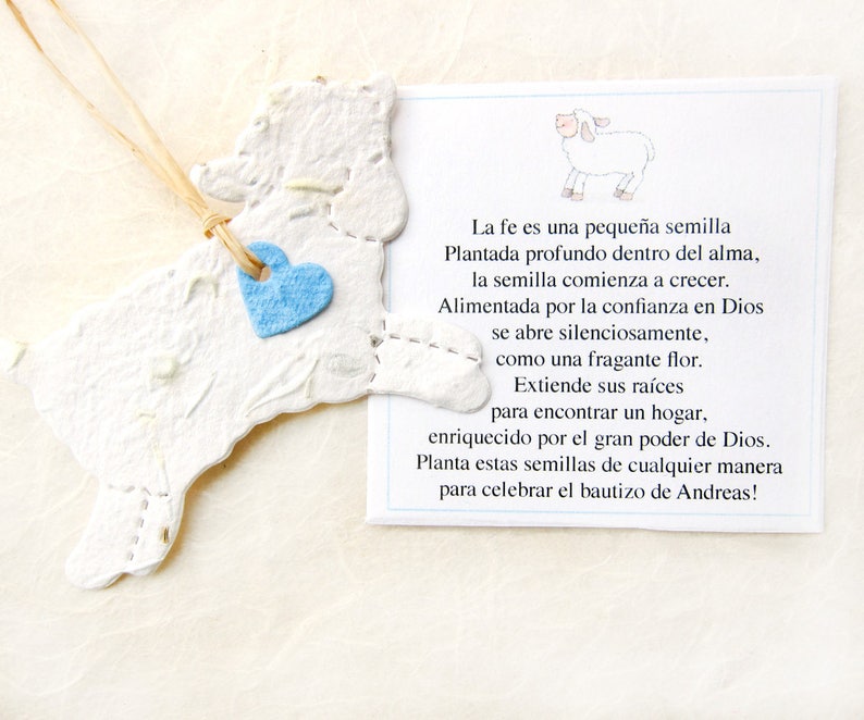 Peut inclure: Un agneau en papier blanc avec un c&oelig;ur bleu attach&eacute;. L'agneau est suspendu &agrave; une ficelle. Le texte sur la carte dit : "La fe es una peque&ntilde;a semilla Plantada profundo dentro del alma, la semilla comienza a crecer. Alimentada por la confianza en Dios se abre silenciosamente, como una fragante flor. Extiende sus ra&iacute;ces para encontrar un hogar, enriquecido por el gran poder de Dios. Planta estas semillas de cualquier manera para celebrar el bautizo de Andreas!"