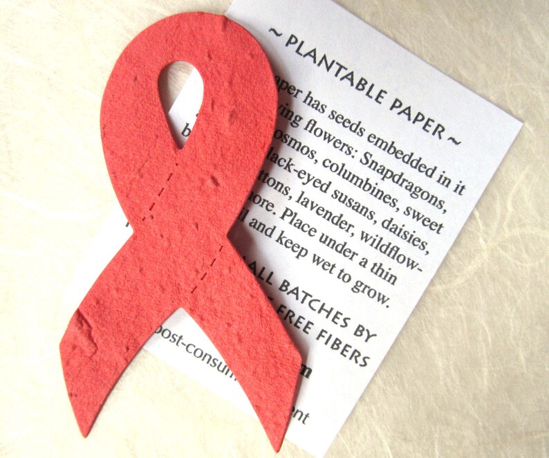 K&ouml;nnte beinhalten: Ein rotes Papierband mit eingebetteten Samen. Das Papier ist mit "Pflanzbares Papier" beschriftet und listet die Arten von Blumen auf, die aus den Samen wachsen werden. Der Text lautet auch "Alle Chargen von Free Fibers".