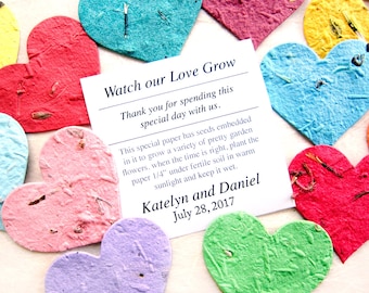 May include: A card with the text "Watch our Love Grow" and "Thank you for spending this special day with us." The card also includes the text "This special paper has seeds embedded in it to grow a variety of pretty garden flowers. When the time is right, plant the paper 1/4" under fertile soil in warm sunlight and keep it wet." The card is surrounded by colorful heart-shaped paper with seeds embedded in them.