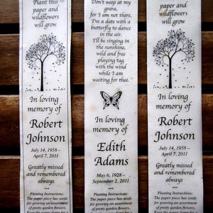 May include: Three white paper bookmarks with black text and illustrations. Each bookmark features a tree with falling leaves, a butterfly, and a message about planting wildflowers in loving memory of a loved one. The text includes the names Robert Johnson, Edith Adams, and Robert Johnson, along with their birth and death dates. The bookmarks also include planting instructions for the wildflower seeds.
