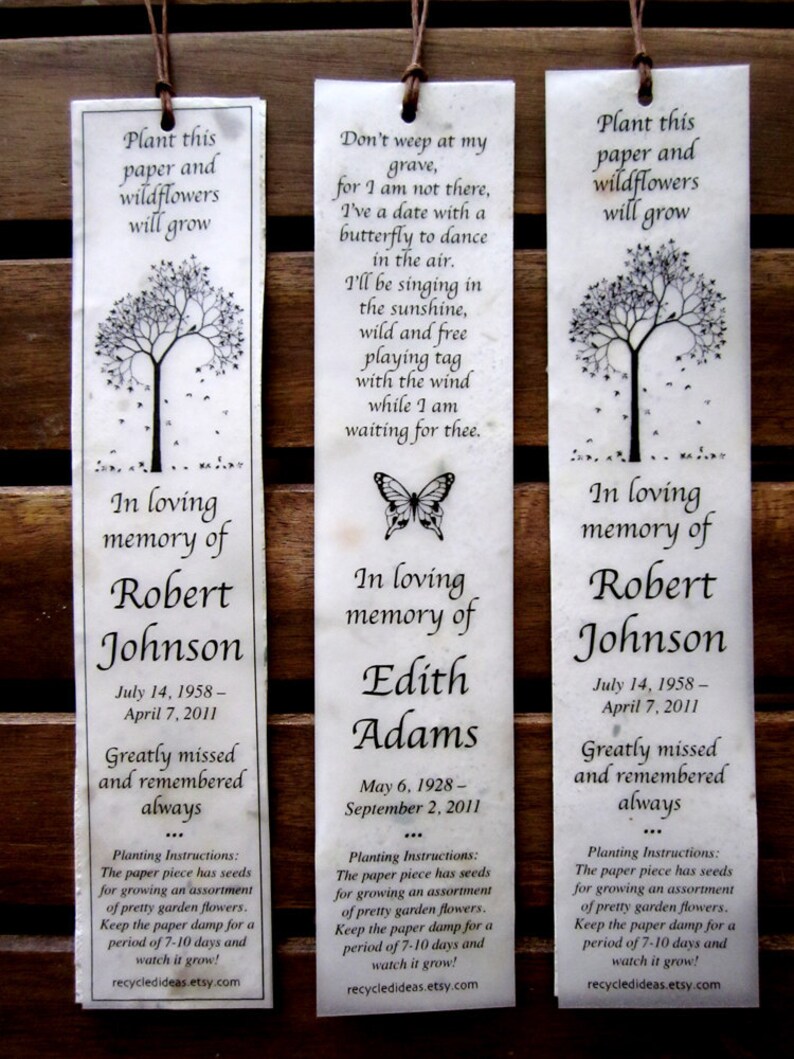 May include: Three white paper bookmarks with black text and illustrations. Each bookmark features a tree with falling leaves, a butterfly, and a message about planting wildflowers in loving memory of a loved one. The text includes the names Robert Johnson, Edith Adams, and Robert Johnson, along with their birth and death dates. The bookmarks also include planting instructions for the wildflower seeds.