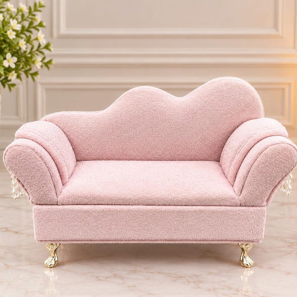 May include: A miniature pink sofa with a textured fabric finish, featuring a curved backrest, rolled arms with hanging crystal-like accents, and four small gold-toned claw-style feet. The piece has a rectangular seat and a scalloped back design.