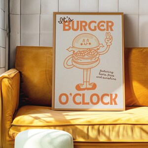 May include: A framed poster with a cartoon burger character with the text "It's Burger O'Clock" and "featuring: beers, fries and sunshine". The poster is on a yellow couch with a light green ottoman in front of it.
