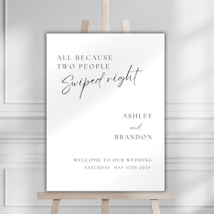 May include: A white wedding sign with black text that reads "All because two people swiped right. Ashley and Brandon. Welcome to our wedding. Saturday May 17th 2025."