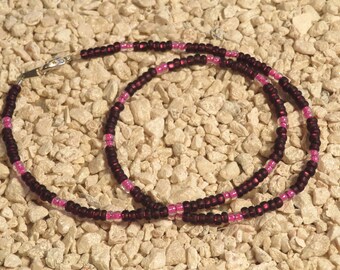 Puede incluir: Un collar de cuentas de color morado oscuro y rosa con un cierre plateado.