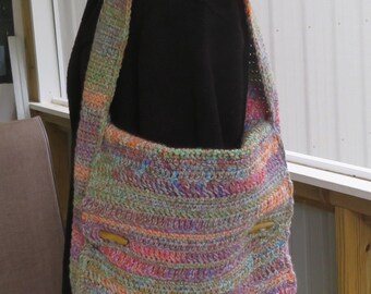 Könnte beinhalten: Handgefertigte, mehrfarbige Häkeltasche. Die Tasche hat eine Mischung aus Pastellfarben, darunter Rosa, Orange, Grün und Blau. Sie hat einen langen Riemen und Holzknopfverschlüsse. Die Tasche wird auf einer Schaufensterpuppe präsentiert.